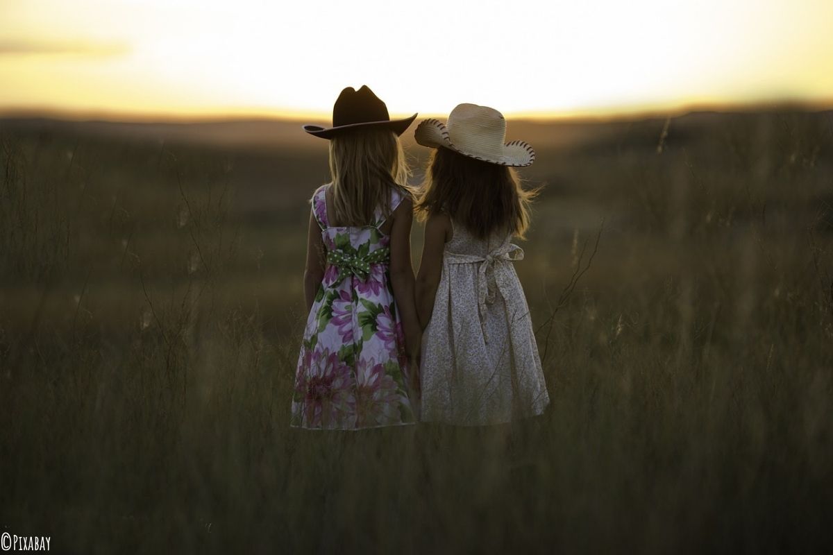 Zwei Mädchen stehen in einem Feld und beobachten den Sonnenuntergang