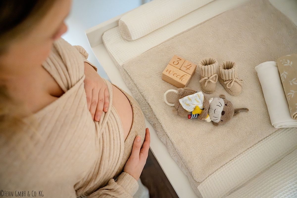 Mama mit Babybauch vor einem Wickeltisch mit Spielzeug Otter