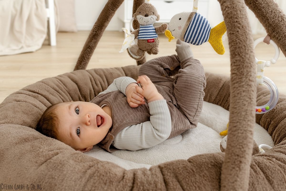 Baby liegt in Babynest mit Mobile und Otter