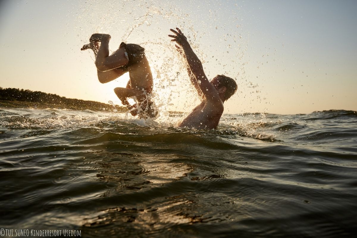 Zwei Personen spielen im Wasser, einer davon macht einen Salto