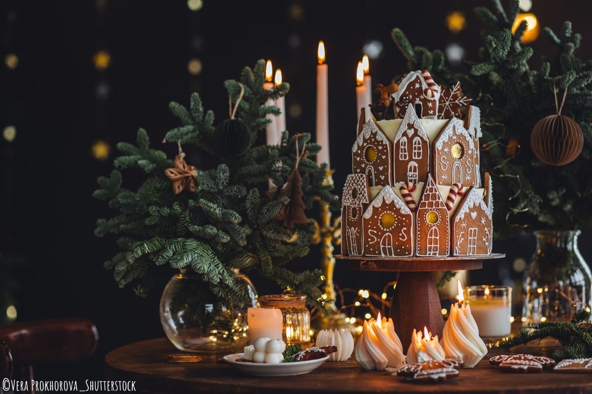 Mehrstöckige Torte, die als Lebkuchenhaus verziert ist, steht auf einem weihnachtlich gedeckten Tisch mit vielen Tannenzweigen