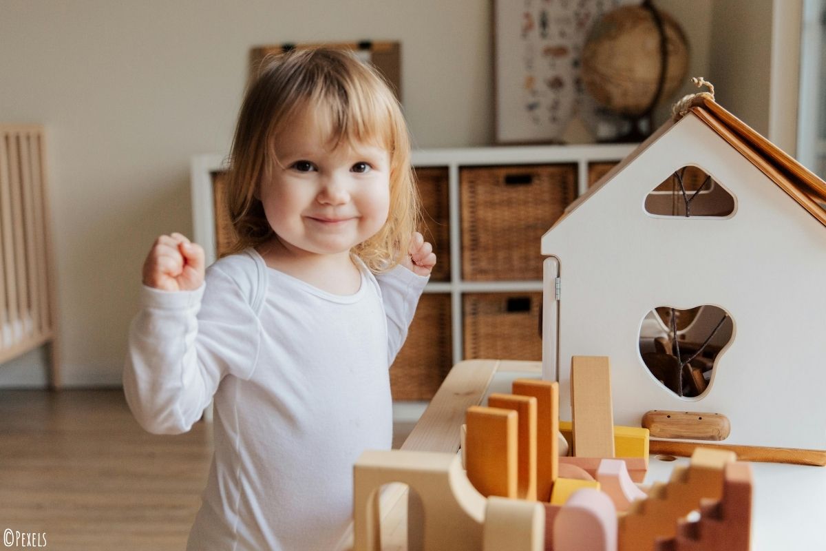 Mädchen spielt in einem Kinderzimmer vor einem weißen Puppenhaus